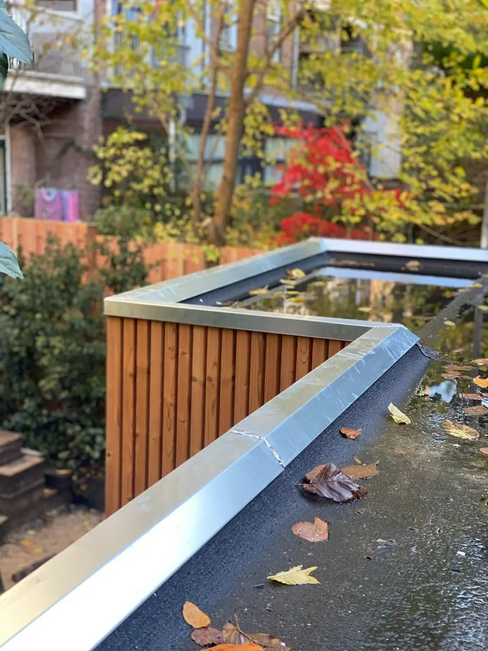 Plat dak van een aanbouw met verse dakbedekking, een gezette metalen dakrand met gesoldeerde hoek, houten gevelbekleding en een lichtstraat.