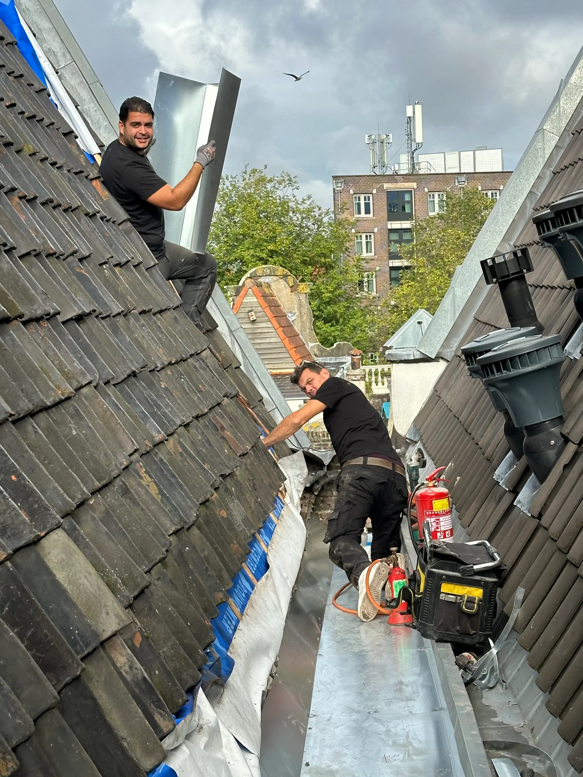 Twee monteurs van LEMA brengen zinkwerk aan op de kap van een Amsterdams grachtenpand.