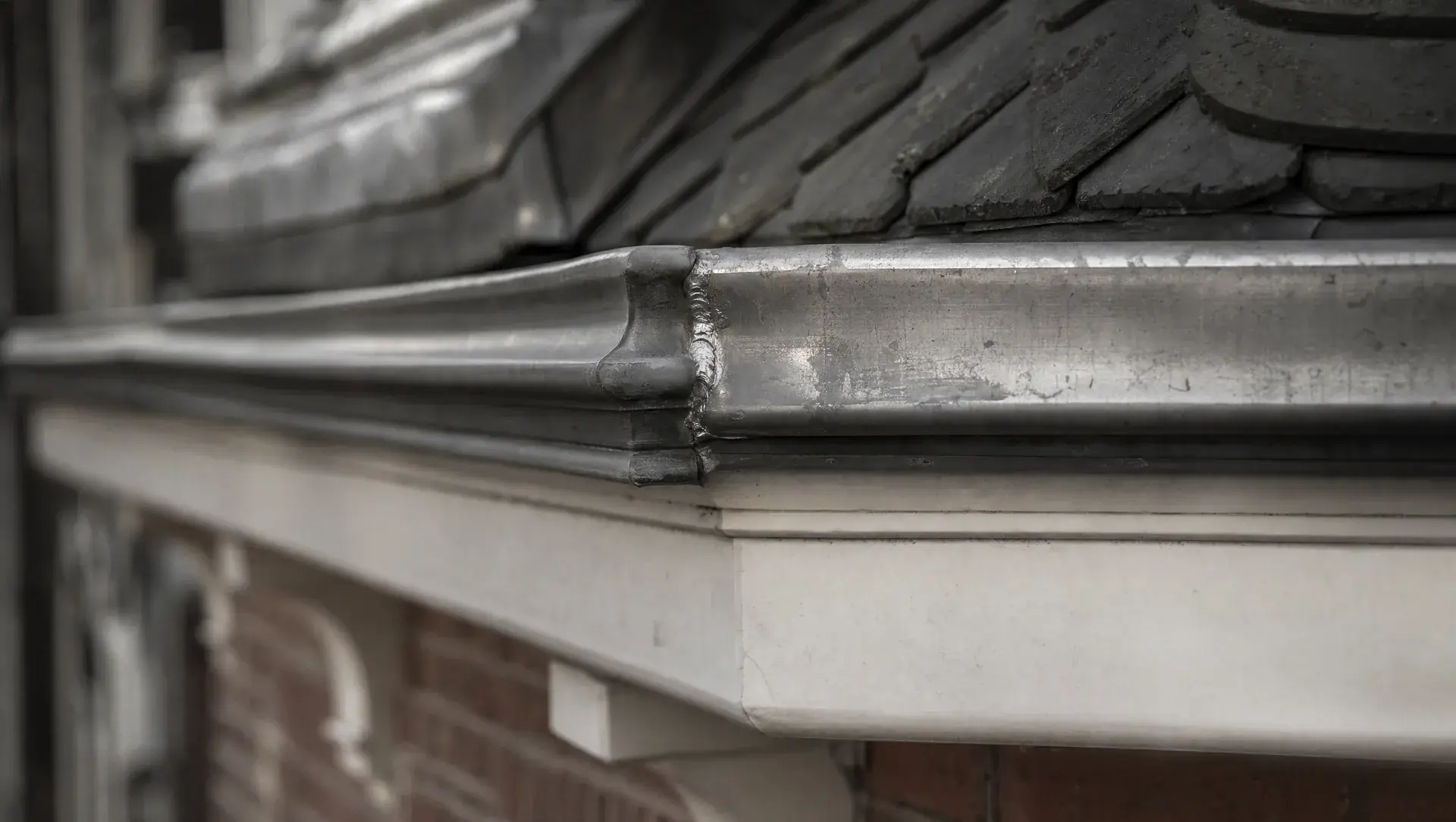 Close-up van een handgezette zinken goot met een verse soldeernaad op de dakrand van een oud pand.